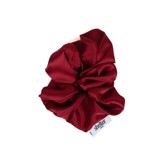 Silk scrunchie in deep red, featuring a soft, luxurious texture and a logo tag.