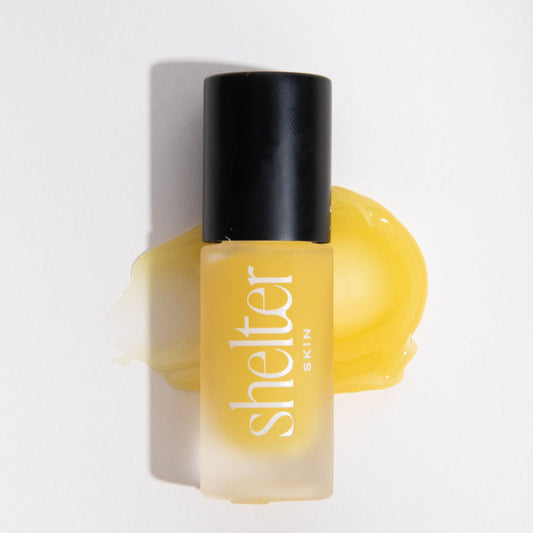 Lanolin Lip Elixir in a frosted bottle with a black cap, surrounded by a yellow lip balm swatch.