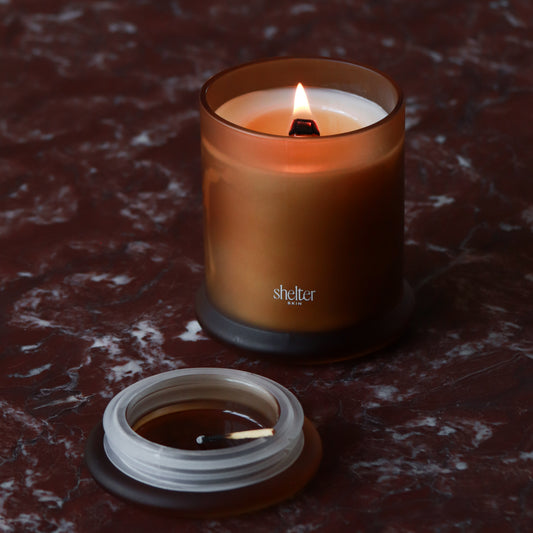 Vanilla Flame Candle in a frosted amber glass jar with a lit wick, resting on a marble surface.